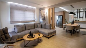 Una sala de estar moderna con un sofá seccional, un comedor con mesa y sillas, y una cocina al fondo.