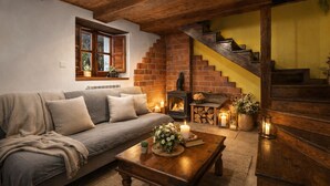 A cozy living room with a sofa, a fireplace, a wooden staircase, and a window with plants. - Congosta, romantic cottage with private jacuzzi in the mountains (Teverga)