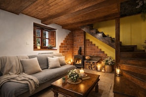 A cozy living room with a sofa, a fireplace, a wooden staircase, and a window with plants.