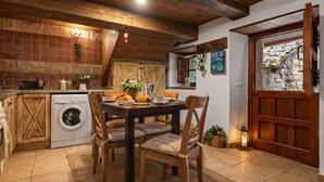 A rustic kitchen with a washing machine, wooden dining table, and chairs. - Congosta, romantic cottage with private jacuzzi in the mountains (Teverga)