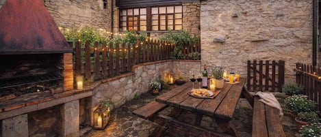 A stone building with a wooden deck, outdoor seating, and a barbecue grill.