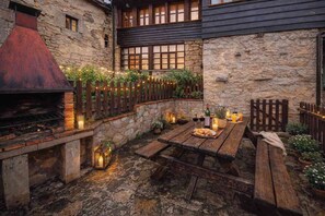 A stone building with a wooden deck, outdoor seating, and a barbecue grill. - Congosta, a romantic cottage with a private hot tub in the mountains (Teverga)