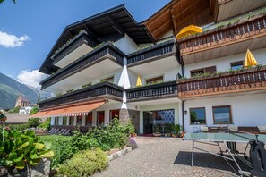Ein mehrstöckiges Gebäude mit Balkonen, einem Tennisplatz und Blick auf die Berge.