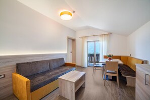 Ein modernes Zimmer mit einer Couch, einem Holztisch, einem Esstisch mit Stühlen und einem Balkon mit Blick.