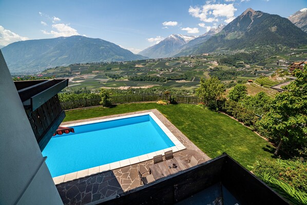 A swimming pool with a stone deck, surrounded by a well-maintained lawn and a view of a mountainous landscape.
