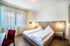 A hotel room with a bed, a desk, a chair, a nightstand with a phone, and a mirror.