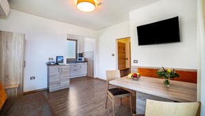 A modern kitchen with a microwave, a dining area with a wooden table and chairs, and a flat-screen TV mounted on the wall. - Apartment "Gartenheim Franz" with Mountain View, Shared Pool & Wi-Fi (Scena)