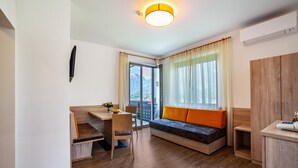 A modern room with a wooden desk, a sofa with orange cushions, a dining table, and a view of mountains through a large window. - Apartment "Gartenheim Franz" with Mountain View, Shared Pool & Wi-Fi (Scena)