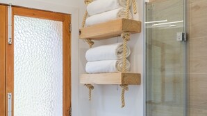 Casa de banho com divisória de chuveiro de vidro, um porta-toalhas de madeira com toalhas e uma janela com vidro jateado.