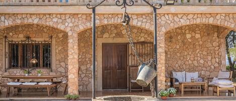 A stone building with a balcony, a stone well, and outdoor seating.