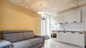Une cuisine moderne avec des meubles blancs, un canapé gris et un luminaire.