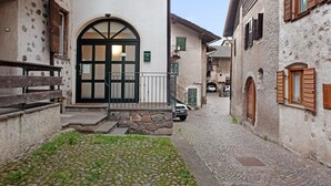 Une ruelle étroite pavée de pierres, bordée de bâtiments historiques, avec un banc en bois et une voiture garée sur le côté.