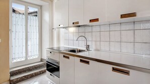 Une cuisine dotée d’un évier en acier inoxydable, de meubles blancs et d’une fenêtre agrémentée d’un rideau.