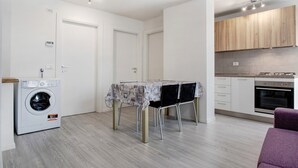 Une cuisine compacte équipée d’un four encastré, d’un lave-linge et d’une table à manger avec des chaises.