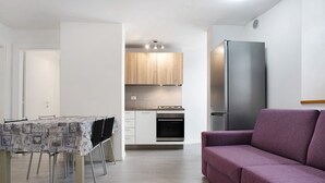 Une cuisine moderne avec des armoires blanches, un réfrigérateur en acier inoxydable et une table à manger avec des chaises.
