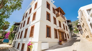 A multi-story building with a white facade and brown window frames, located on a cobblestone street with a mountain in the background.