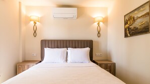 A hotel room with a large bed, two bedside tables, a wall-mounted air conditioner, and two wall-mounted lamps.
