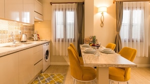 A modern kitchen with white cabinets, a washing machine, and a dining area with a marble table and yellow chairs.