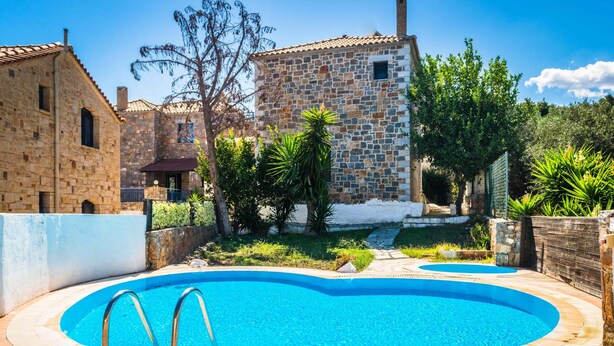 A swimming pool with stone buildings in the background. - Niriides Villas | Nisso | Villa 2-bedrooms with private pool (CHERSONISSOS-HERAKLION)