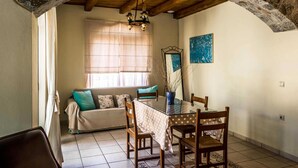 A dining area with a wooden table, chairs, and a sofa. - Niriides Villas | Nisso | Villa 2-bedrooms with private pool (CHERSONISSOS-HERAKLION)