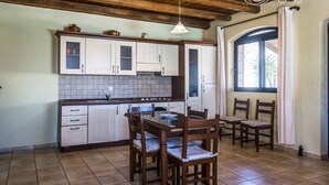 A kitchen with wooden cabinets, a tiled backsplash, a dining table with chairs, and a chandelier. - Niriides Villas | Liagori | Villa 2-bedrooms with private pool (CHERSONISSOS-HERAKLION)