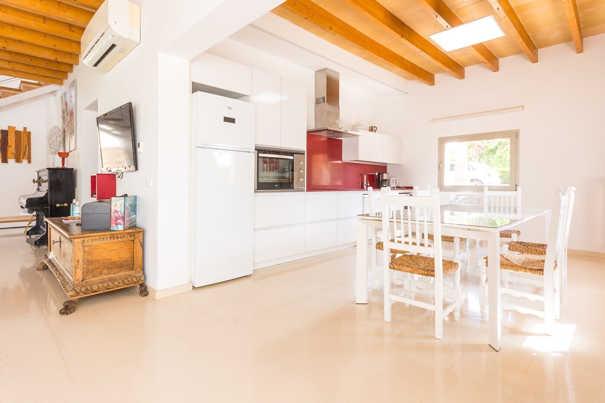 Une cuisine moderne avec des meubles blancs, un plan de travail rouge et un coin repas avec des chaises blanches.