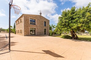 Un bâtiment en pierre avec un panier de basket, un arbre et un ciel dégagé.