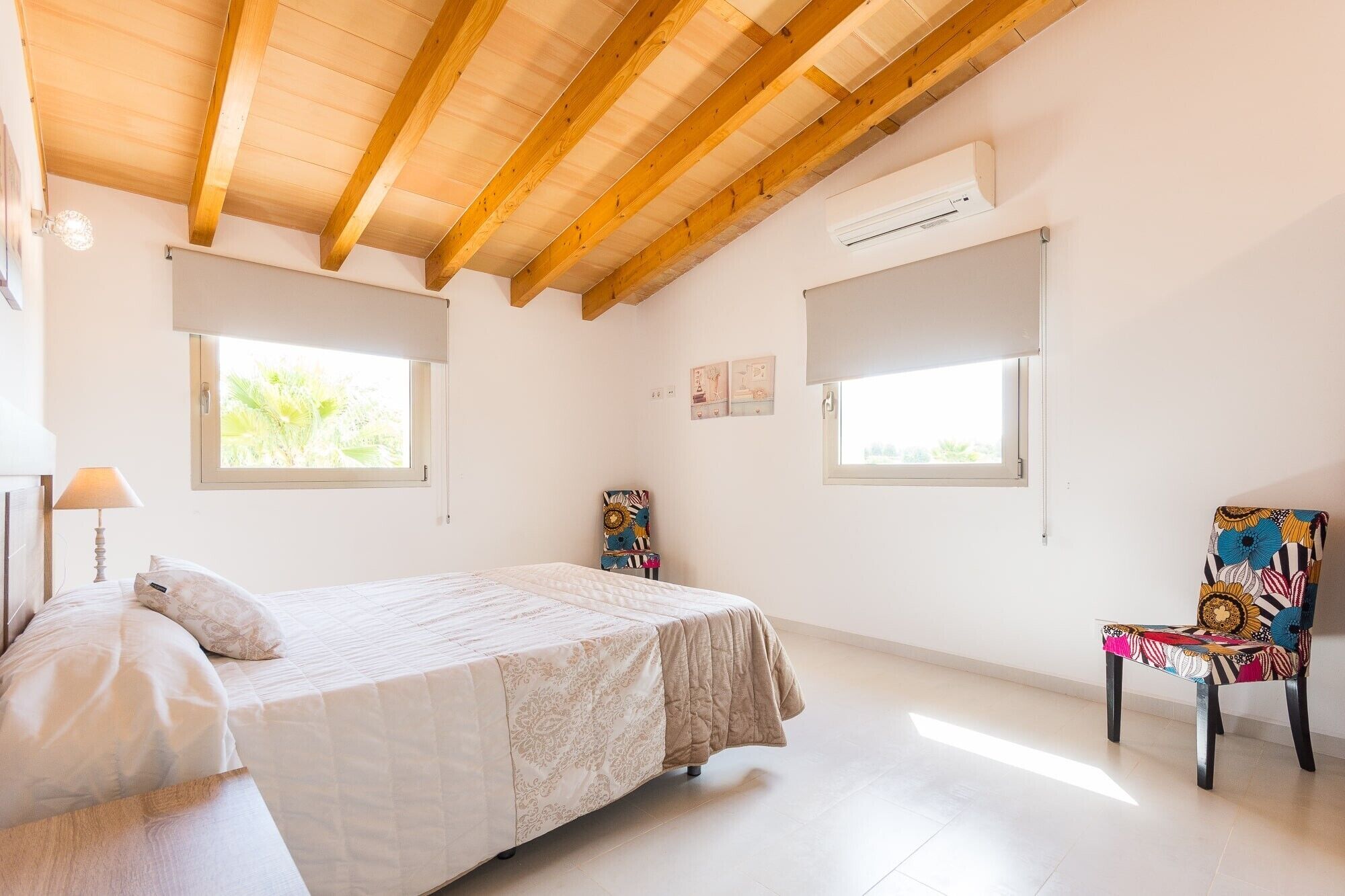 A bedroom with a bed, two windows, an air conditioning unit, and a chair.