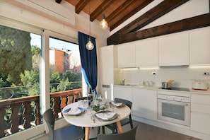 A modern kitchen with a built-in oven, a dining table set for four, and a view of the outdoors through a large window.