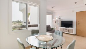 Ett modernt vardagsrum med ett matbord i glas, en soffa, en tv och ett stort fönster.