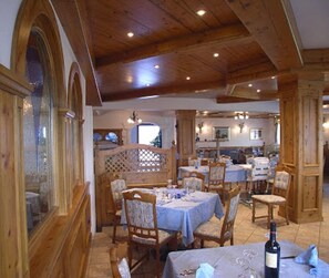A restaurant with wooden beams, tables set for dining, and a wine bottle on the table.
