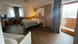 Habitación de hotel con cama, escritorio, silla, una mesita y un ventanal con cortinas.