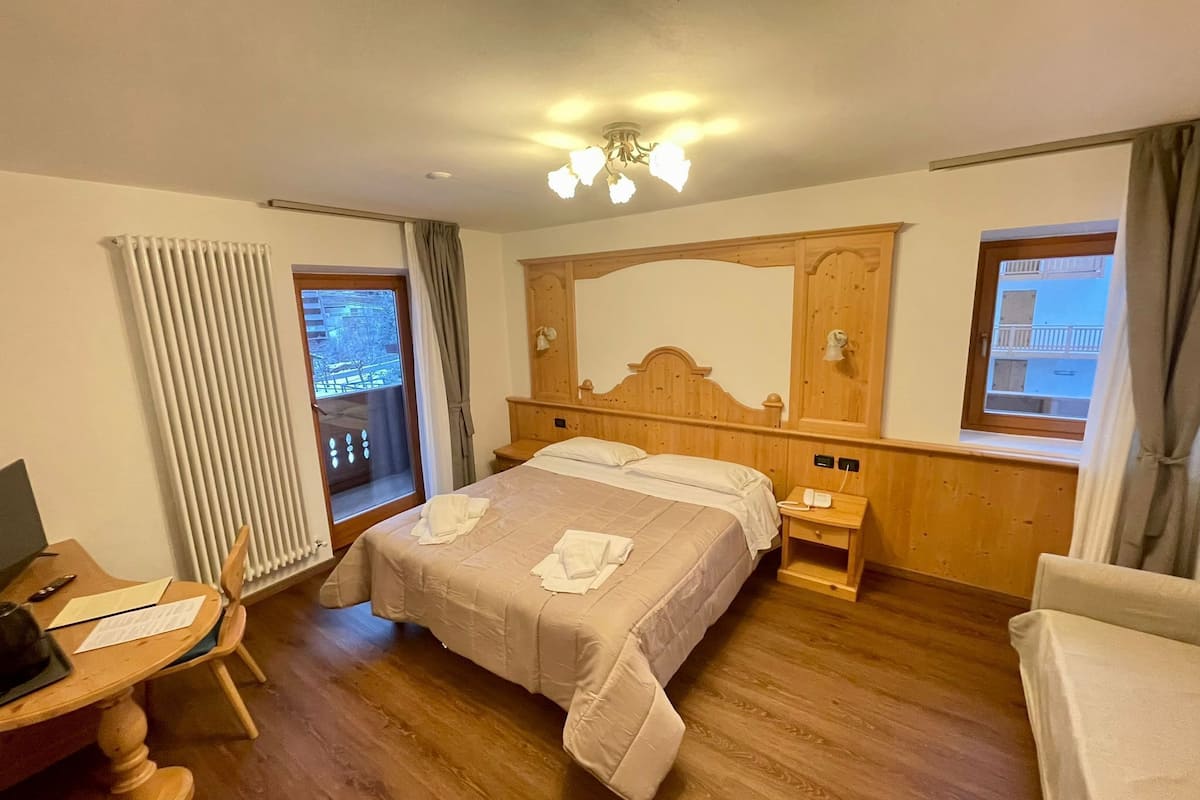 Ein Hotelzimmer mit einem hölzernen Bett, einem Schreibtisch mit Stuhl, einem Nachttisch und einem Fenster mit Vorhängen.