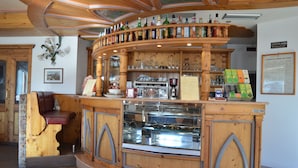 Un área con barra de madera, una vitrina de vidrio, un banco y varios botellas y copas en estantes.