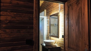 A wooden cabin interior with a bathroom featuring a white sink, a mirror, and a wooden door. - Glamping Büyükada (Adalar)