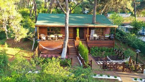 A wooden cabin with a green roof, surrounded by lush greenery and a deck with outdoor seating. - Glamping Büyükada (Adalar)