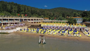 A beach resort with rows of sun loungers and umbrellas, a swimming pool, and a building with multiple balconies. - Glamping Büyükada (Adalar)