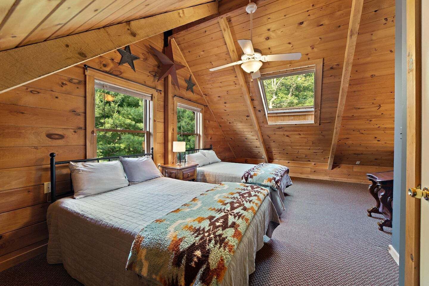 Une chambre confortable située dans les combles, avec deux lits, un ventilateur de plafond et de grandes fenêtres donnant sur un paysage verdoyant.