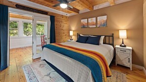 Une chambre à coucher avec un lit, des tables de chevet, un ventilateur de plafond et une vue sur l’extérieur.