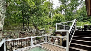 Un bain à remous sur une terrasse en bois, entouré d’une rambarde métallique, avec un escalier menant à un niveau supérieur.