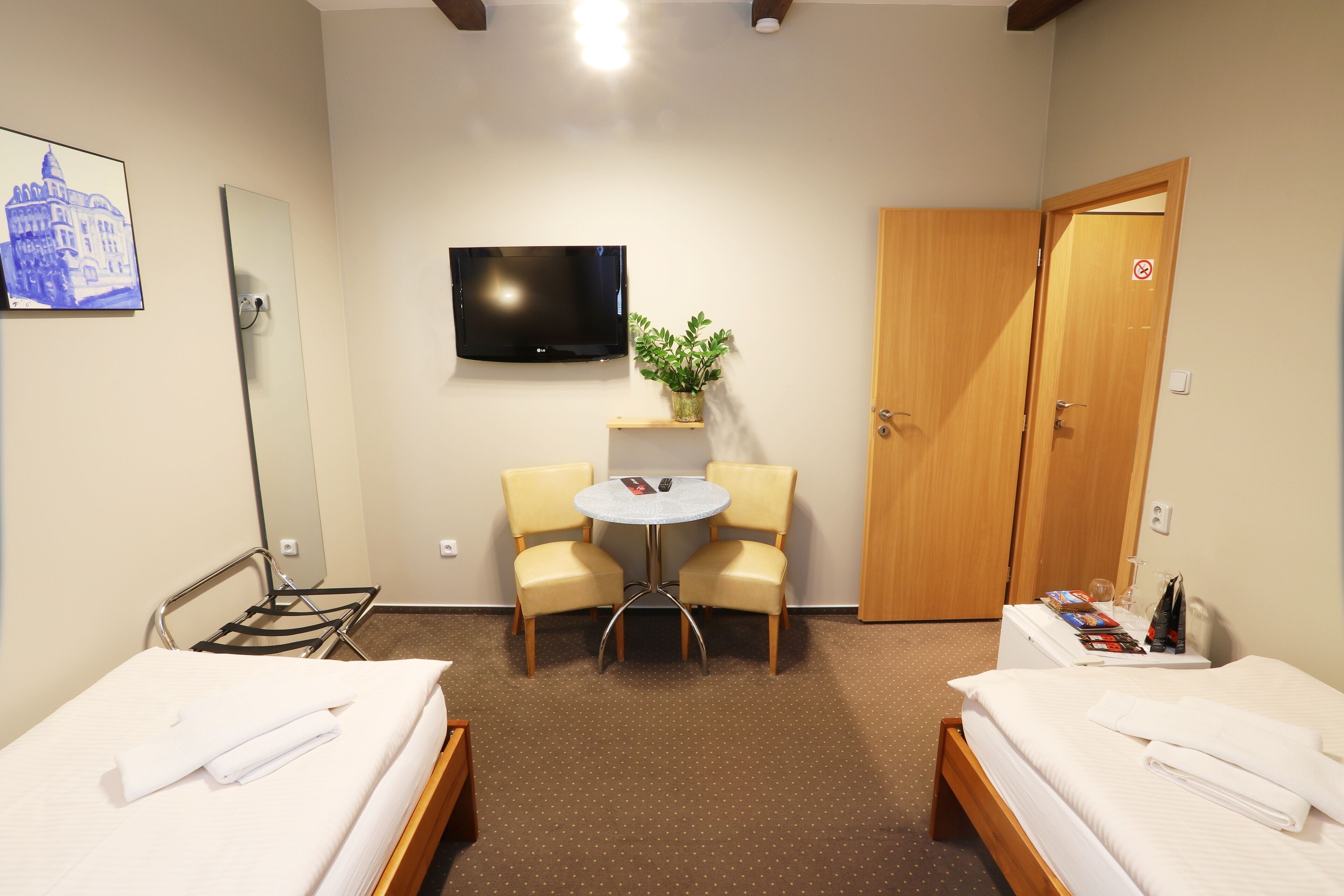 A hotel room with two beds, a TV, a small table with chairs, a potted plant, and a wooden door.