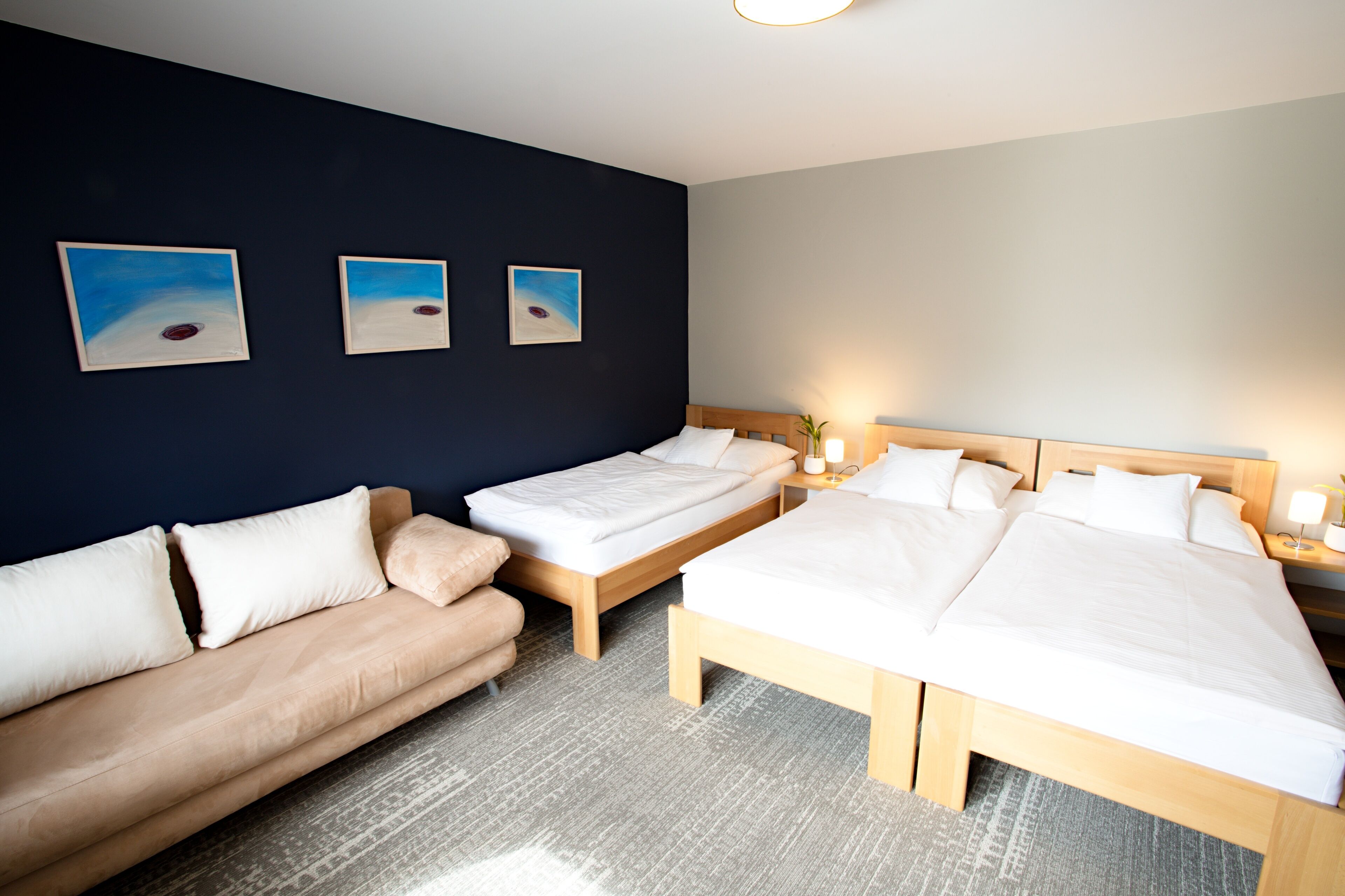A hotel room with a bed, a sofa, and three paintings on the wall.