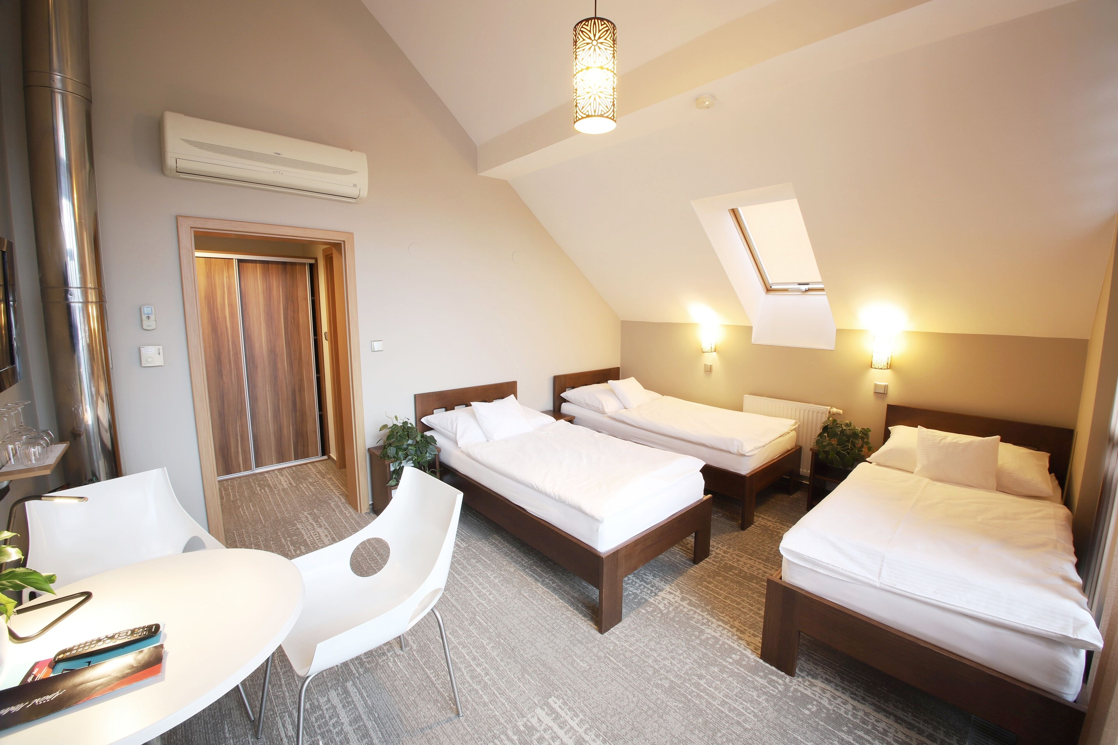 Een hotelkamer met twee eenpersoonsbedden, een bureau met stoel, een klein tafeltje en een plafondlamp.