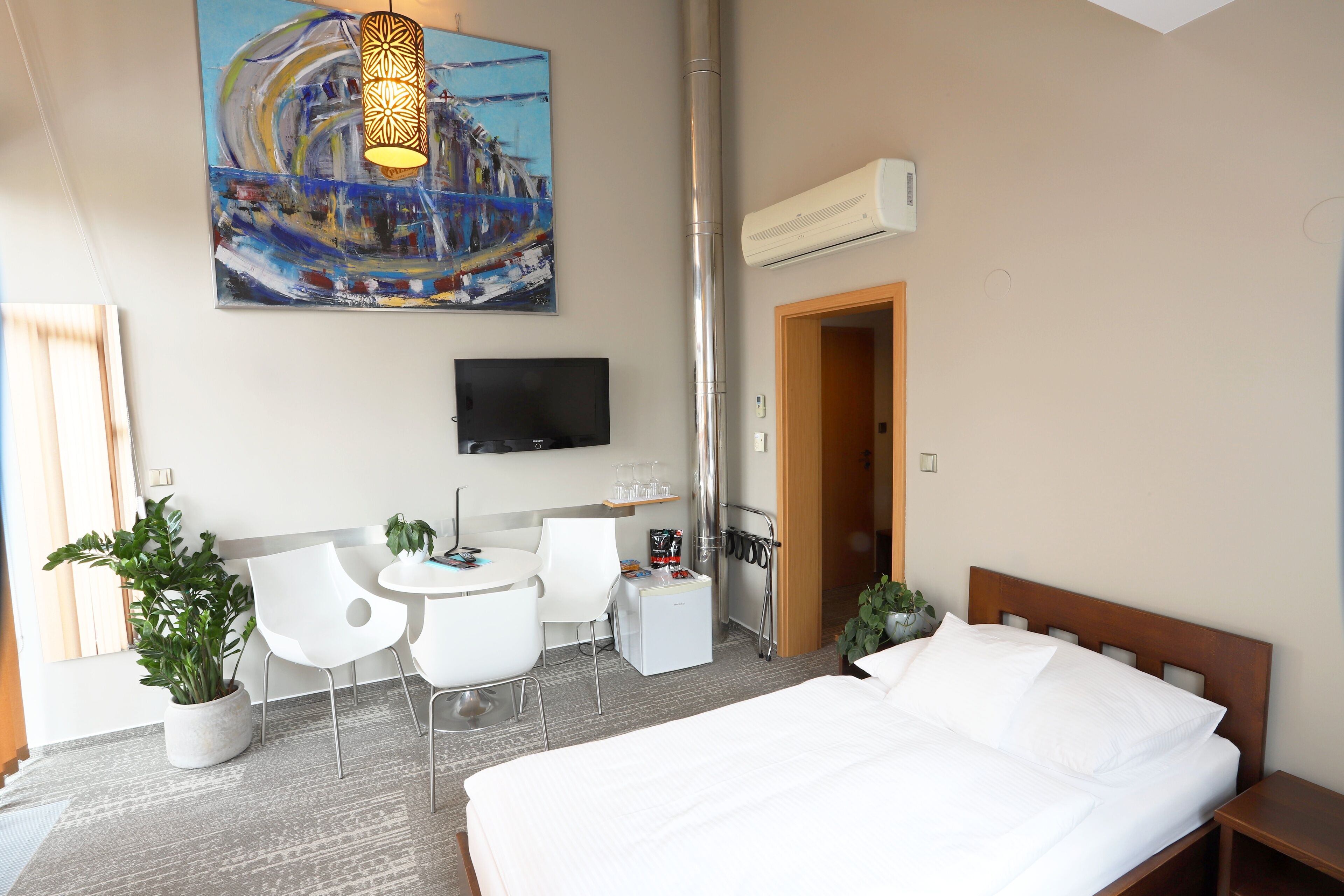Hotelkamer met een bed, een bureau met stoel, een televisie, een bloempot en een schilderij aan de muur.