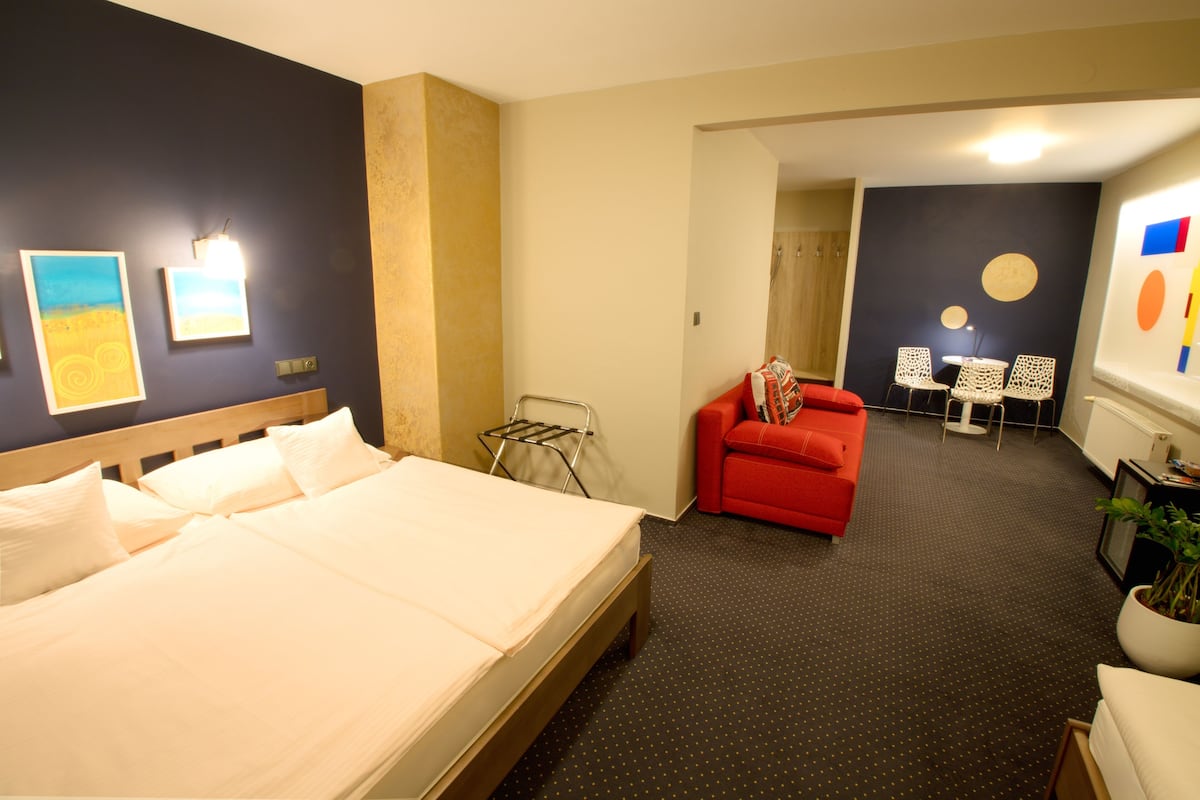 Una camera d'albergo con un letto grande, un divano rosso, un tavolino e delle sedie.