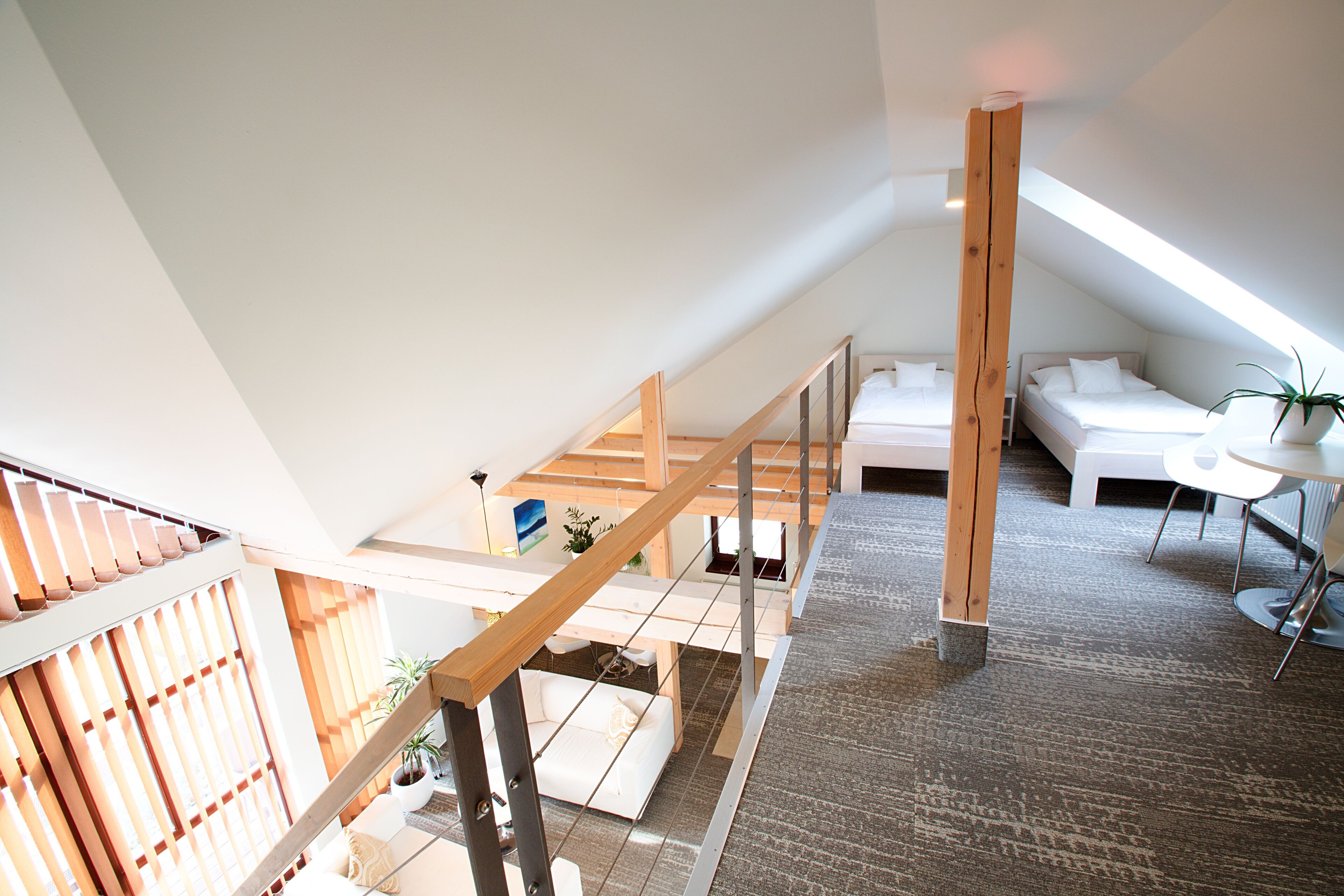 Een slaapkamer in loftstijl met een schuine kap, een houten trap, een witte bank en een kleine tafel met een plant.