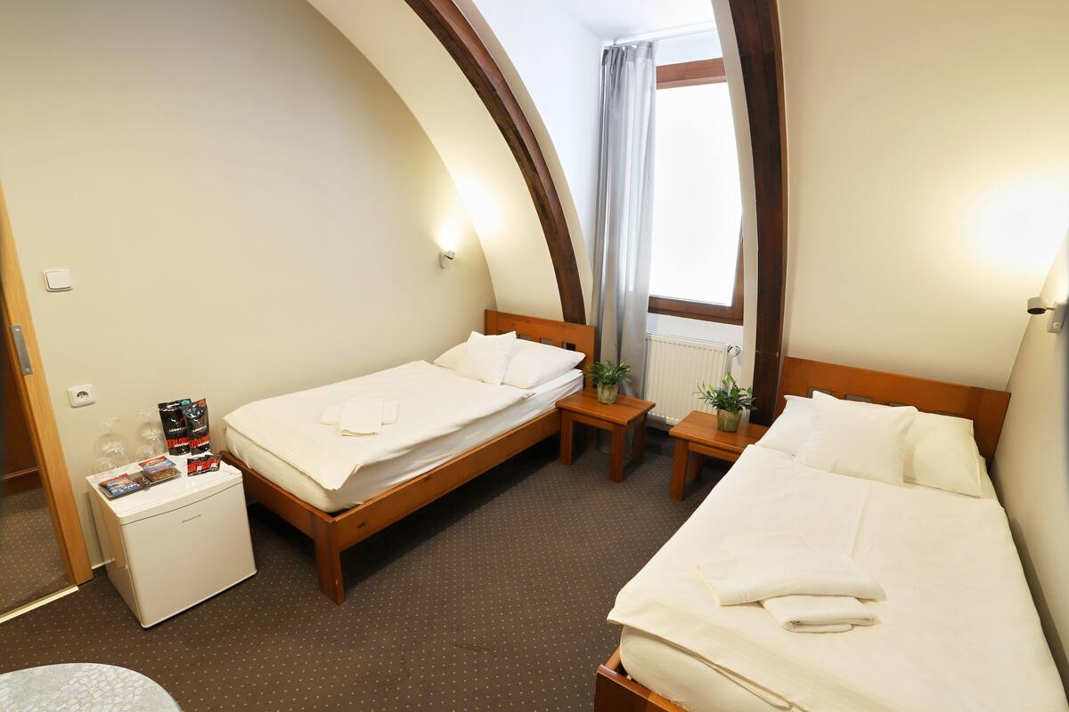 Camera d'albergo con due letti, una piccola scrivania, un frigorifero e una finestra con tende.