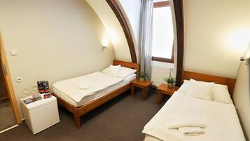 A hotel room with two beds, a small desk, a refrigerator, and a window with curtains.
