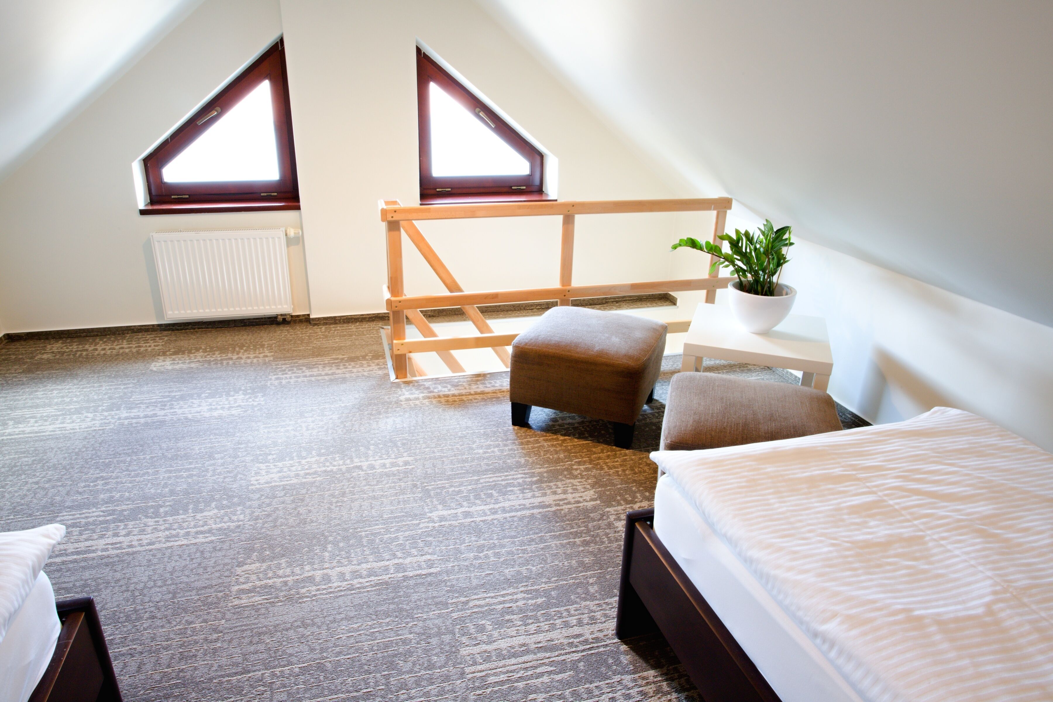 A room with a sloped ceiling, two windows, a bed, a chair, a small table, and a potted plant.