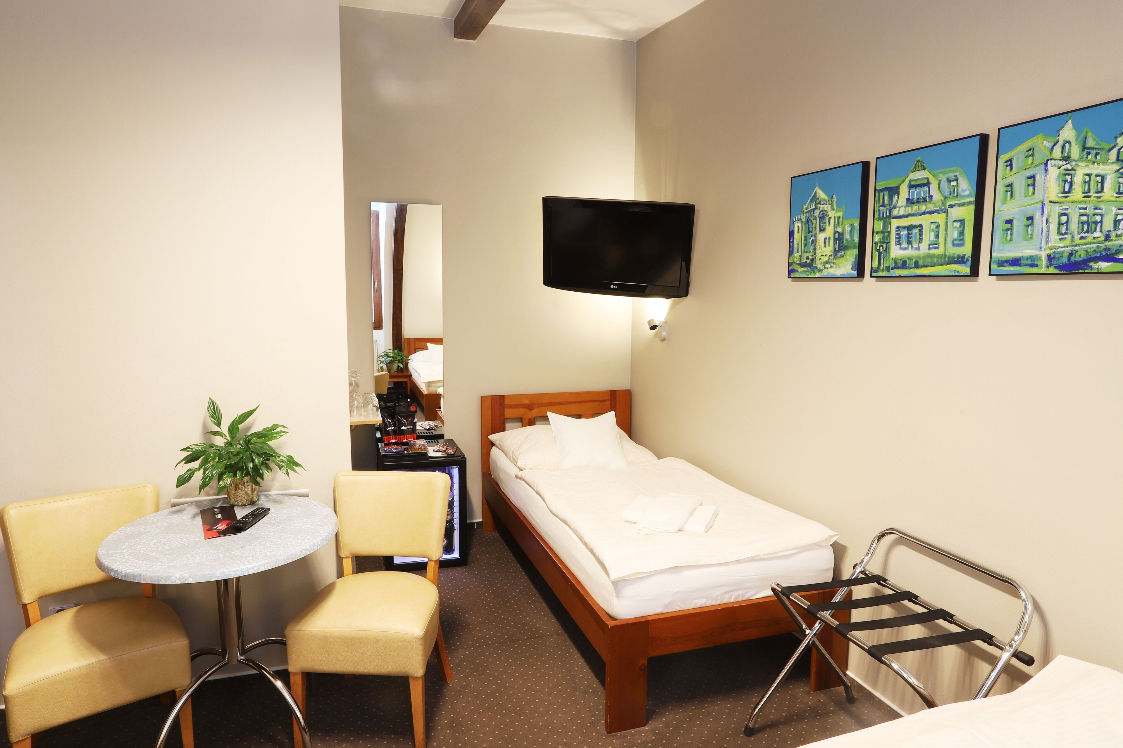 Habitación de hotel con cama, televisor montado en la pared, una mesita redonda con sillas y una planta.